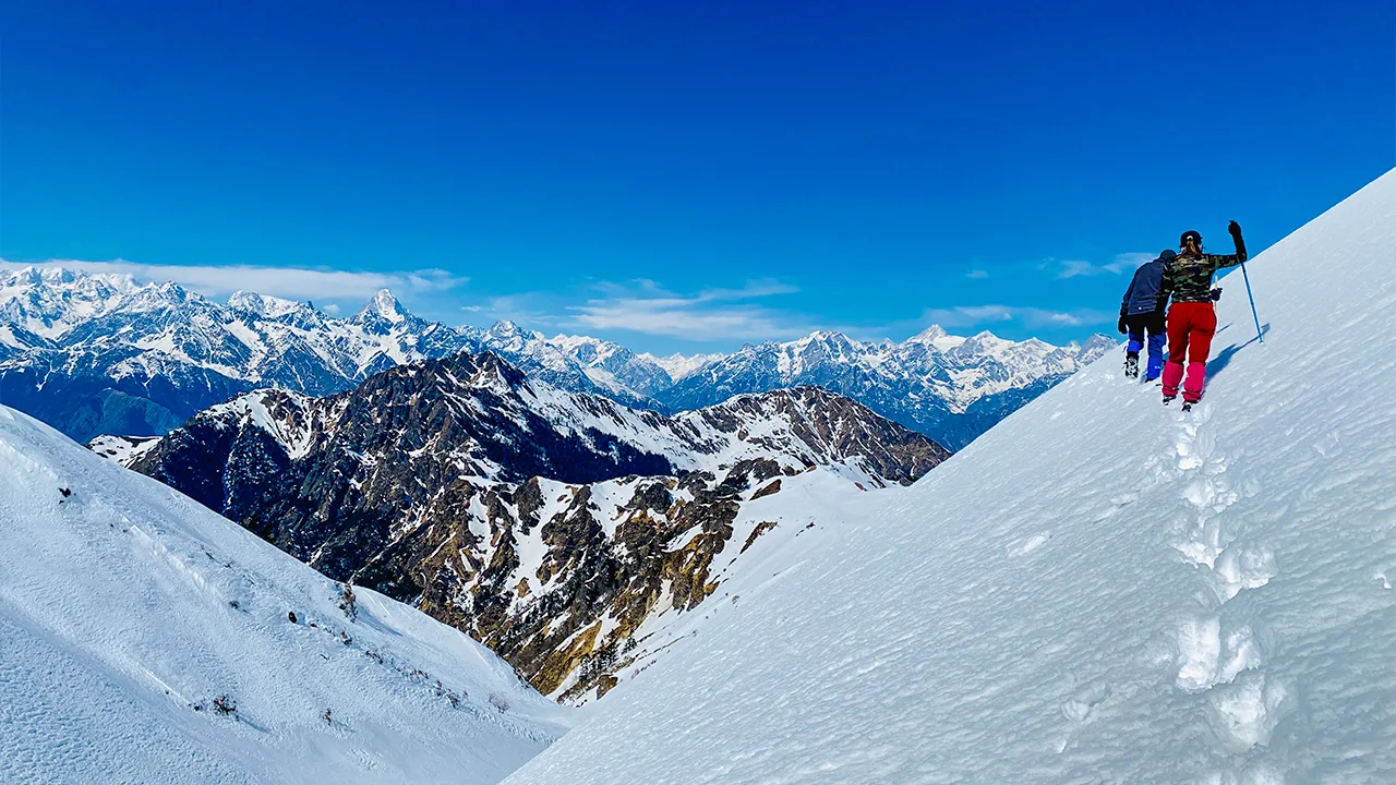 Trekkers hiking in India on a snow-covered mountain trail, surrounded by majestic Himalayan peaks under a clear blue sky