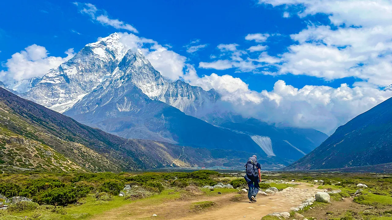 Trekker walking on scenic mountain trail in Nepal with stunning views of snow-capped Himalayan peaks during a high-altitude hiking adventure, Trek The Himalayas